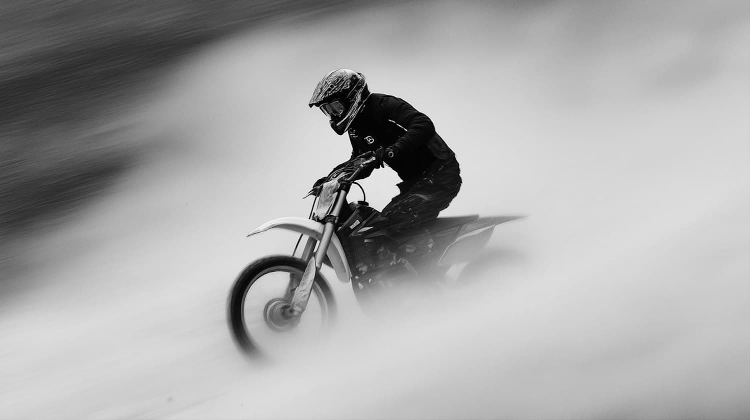 Rider on a dirt bike leaning through a cloud of dust